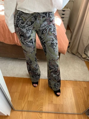 Vintage mönstrade bootcut byxor - Lågmidjade bootcut byxor med paisley-inspirerat mönster i grönt, svart och grått.  Storlek 40, liten i storleken! Märke: Panos emporio