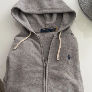 Grå hoodie från Polo Ralph Lauren - Zip hoodie från Polo Ralph Lauren i färgen grå. Hoodien är nästan helt ny passar som bäst mellan 170-183cm. Bara att höra av sig vid funderingar. Kan eventuellt tänka mig att gå ner lite i pris vid snabb affär 
