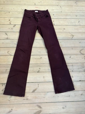 Mörklila bootcut jeans - Säljer ett par vinröda bootcut jeans med klassisk femficksdesign. Jeansen har utsvängda ben och är tillverkade i ett mjukt bomullsmaterial med lite stretch. Perfekta för dig som vill ha en retro och unik look.