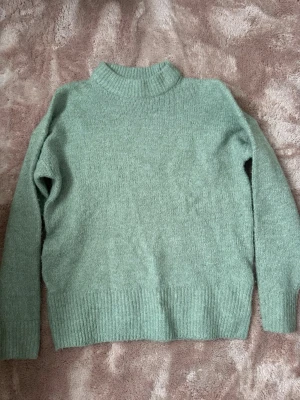 Grön stickad tröja - Mysig stickad tröja i ljusgrönt med långa ärmar. Tröjan har ribbstickade muddar vid hals, ärmslut och nederkant. Perfekt för kyliga dagar och enkel att matcha med jeans eller kjol.