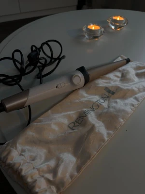 Remington locktång konisk vit/grå - Säljer en konisk locktång från Remington i vit och grå färg med svart detalj. Tången har en sladd och medföljer en skyddande tygpåse i ljusbeige. Perfekt för att skapa snygga lockar och vågor i håret. Värmehandske medföljer.