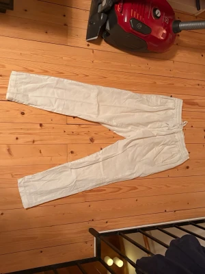 Vita linnebyxor med dragsko - Säljer ett par vita linnebyxor med avslappnad passform och elastisk midja med dragsko. Byxorna har raka ben och fickor både fram och bak. Perfekta för en chill och stilren look.