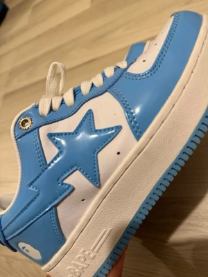 BAPE STA blå och vita sneakers - Säljer ett par BAPE STA sneakers i blankt blått och vitt läder. Skorna har den ikoniska stjärnan på sidan, vita snören och en blå sula. Perfekt för dig som vill sticka ut med streetwear-vibe och snygg design. US 6 i storlek