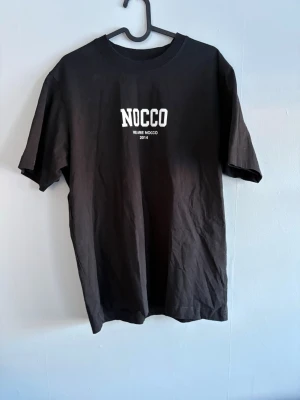 Svart NOCCO t-shirt med tryck - Svart t-shirt från NOCCO med stilrent vitt tryck fram och bak. Bekväm passform och skönt material, passar perfekt både till vardag och träning. Är i storlek S men passar också perfekt till någon med storlek M