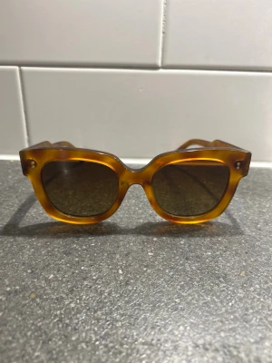 Bruna fyrkantiga solglasögon - Snygga solglasögon med fyrkantig form och brunmelerad båge. Glasen är mörka och bågarna har en retrovibe som passar perfekt till sommaren. Tillverkade i syntetmaterial och ger en cool look till alla outfits.