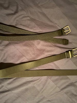Två olivgröna bälten med metallspänne - Säljer två snygga svarta bälten, ett i flätad textil från Jack and Jones på 105cm och ett i slätt konstläder som jag inte vet vart den kommer ifrån på 120cm. Båda har stilrena metallspännen i silverfärg. Perfekta för att lyfta din outfit med en enkel detalj. Passar till jeans, kjol eller byxor. Skriv till mig om du funderar på att köpa en av dom.