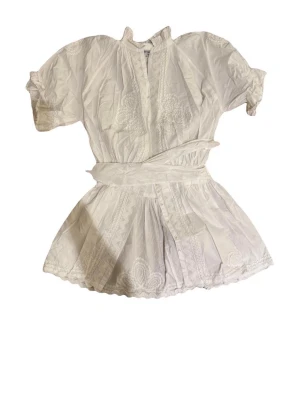 Vit broderad blus med knytband - Så fin klänning från Juliett Dunn, med broderade detaljer och korta puffärmar. Det är storlek 2 men skulle säga att det motsvarar en S/M. Säljer då den tyvärr inte passar