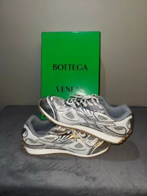 Bottega Orbit - Snygga Bottega Orbit i silver och vitt med coola meshdetaljer och svarta grafiska linjer. Skorna har snörning och en chunky sula som ger en modern vibe. Perfekta för dig som vill sticka ut med exklusiv design. Skriv för mer information.
