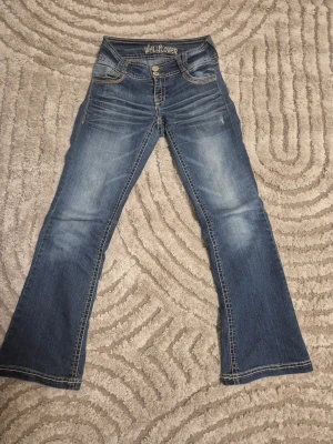 Blå low waist bootcut jeans från Wallflower - Säljer ett par blå bootcut jeans från Wallflower med snygga slitningar och kontrastsömmar. Jeansen har låg midja, fem fickor och dekorativa bakfickor med knappar. Storlek 32 - 34. Perfekta för dig som gillar en avslappnad men trendig stil. Ställ gärna frågor om pris eller byxa!❤️