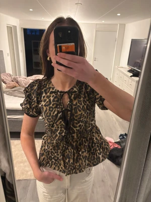 Leopardmönstrad blus med rosett - Snygg blus med leopardmönster och korta puffärmar. Blusen har två knytband framtill. Älskar den men har tyvärr inte kommit till användning. Sitter som s och xs