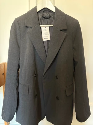 Mörkgrå kavaj från BikBok - Stilren mörkgrå kavaj från BikBok med dubbelknäppning och två fickor framtill. Aldrig använd med prislappen kvar. Oversize i storleken