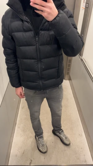 Svart pufferjacka med huva - Kan diskuteras vid snabbaffär!!!Säljer en svart pufferjacka med huva och dragkedja framtill. Jackan har en stilren look med breda, vadderade paneler och två sidofickor. Perfekt för kalla dagar och ger en modern streetwear-vibe.