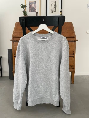 Grå sweatshirt från Weekday - En stilren grå sweatshirt från Weekday i mjuk bomullsblandning. Klassisk rund halsringning, ribbade muddar vid ärmslut och nederkant. Perfekt basplagg för en avslappnad och trendig look.