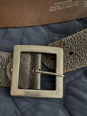 Svart bälte  i skinn från Bernd Götz - Snyggt svart bälte i äkta skinn från Bernd Götz med grov textur och fyrkantigt metallspänne. Perfekt för att ge din outfit en cool touch. Tillverkat i Tyskland och har en robust känsla.