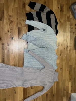Fyra stickade tröjor och klänning - Fyra stickade plagg: en svart-beige randig tröja, två ljusgrå tröjor och en lång beige ribbstickad poloklänning. Alla har lång ärm och mjuk, mysig känsla. Perfekta för lager-på-lager och stilrena outfits. 