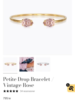 Petite Drop armband Vintage Rose - Stilrent armband i guldton med två droppformade rosa stenar i varje ände. Armbandet har en öppen design och gnistrar snyggt tack vare de slipade stenarna. Perfekt accessoar för att lyfta din outfit med en touch av vintagekänsla och elegans.