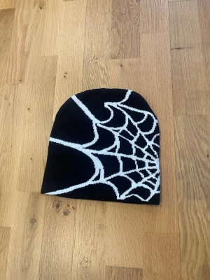 Svart mössa spindelnät  - Svart mössa med spindelnätsmotiv. Mjuk och stretchig perfekt till skidåkning eller vardagsmode. 