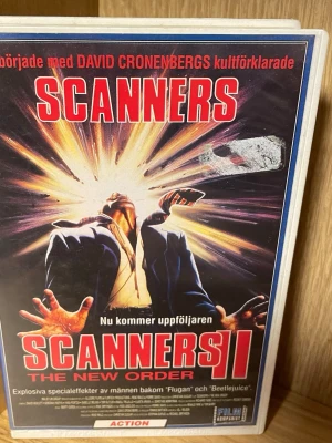 Scanners II: The New Order VHS - Säljer boken 'Scanners II: The New Order' med ett dramatiskt omslag i rött, svart och gult. Omslaget har en explosion och en person i kostym. Filmen  är på svenska och har actiontema med inslag av science fiction och övernaturliga krafter.