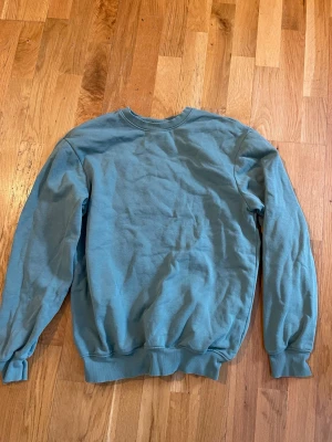 Blå crewneck sweatshirt - En enkel blå crewneck sweatshirt med rund hals och ribbade muddar vid ärmslut och nederkant. Perfekt för en avslappnad stil och lätt att matcha med jeans eller joggers. Materialet känns mjukt och bekvämt.