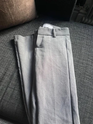 Grå kostymbyxor från Bershka - Snygga grå kostymbyxor från Bershka som inte säljs längre. De är i en storlek 32 💗 Tyvärr har ett utav ”spännena” lossnat, som man kan se på bild, utöver det är dom som ny