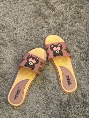 Rosa tofflor med nallemotiv - Ett par söta tofflor köpta utomlands så du hittar inte dessa i Sverige. Perfekta för att chilla hemma eller på sommaren. Står att de är storlek 41 men detta är inte i EU. 39-40 i EU storlek. 