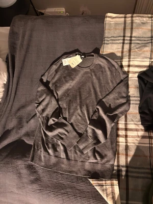 Mörkgrå merinoullströja från Uniqlo - Snygg och stilren mörkgrå stickad tröja från Uniqlo i extra fin merinoull. Tröjan har rund halsringning, långa ärmar och ribbade muddar. Perfekt för lager-på-lager och enkel att tvätta i maskin.