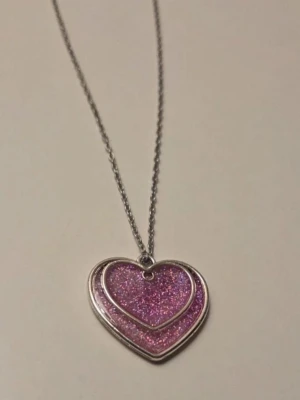 💖 Sparkly Double Heart – Handgjort halsband i stål - Hänget är fyllt med ett magiskt rosa glitter som skyddas av en glashärdad emaljfinish. Det ger en lyxig, blank yta med ett fantastiskt djup som verkligen poppar i ljuset! Perfekt som en romantisk present eller för att ge din egen outfit lite extra sparkle. Detaljer: Design: Dubbelt hjärta med rosa glitter & glashärdad yta. Material: Kedja i högkvalitativt rostfritt stål – hållbart, allergivänligt och tappar inte färgen. Storlek: Hänget är ca 2,5 cm. Kedjan är ca 45 cm. Skick: Nytt/Egentillverkat