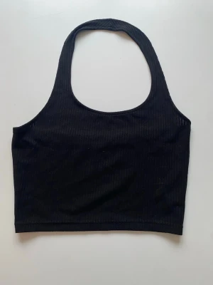 Svart ribbad croppad linnetopp - Snygg svart croppad linnetopp med ribbad struktur och breda axelband. Toppen har en enkel och stilren design som passar perfekt till jeans eller kjol. Materialet känns mjukt och stretchigt, vilket gör den bekväm att bära.