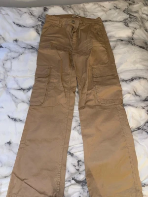 Beiga cargobyxor med stora fickor - Säljer ett par beiga cargobyxor med bred passform och stora sidofickor. Byxorna har klassisk cargostil med flera fickor. Perfekta för en avslappnad streetwear-look. 