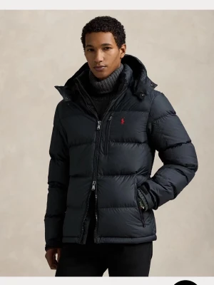 Svart pufferjacka från Polo Ralph Lauren - Snygg svart pufferjacka från Polo Ralph Lauren med röd logga på bröstet. Jackan har hög krage, avtagbar huva och dragkedja framtill. Fylld med dunliknande material för extra värme och har flera praktiska fickor.