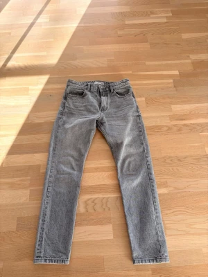 Grå raka jeans i vintage-look - Säljer ett par grå jeans med rak passform och klassisk femficksdesign. Jeansen har en snygg tvättad vintage-look och normal midja. Perfekta för dig som gillar en avslappnad men stilren stil. Materialet är bomull och de har dragkedjegylf.