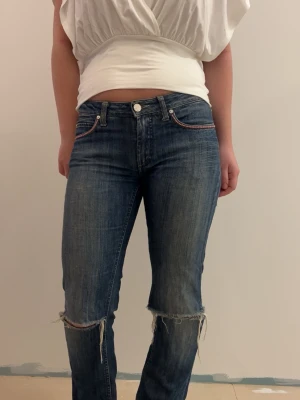 Blå slitna jeans med raka ben - blå jeans från Acne med raka ben och slitna detaljer vid knäna. Jeansen har klassisk femficksdesign och handsydda pärlor upptill vid fickorna. Perfekta för en avslappnad och trendig look💙😊.