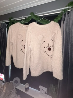 Beige fleece-tröja med Nalle Puh - Supermysiga beige loungewear-tröjor i fluffigt fleece-material med Nalle Puhs ansikte broderat framtill och söta öron på axlarna. Perfekt för chillkvällar hemma och riktigt skön att ha på sig när det är kallt. En i L och en i M