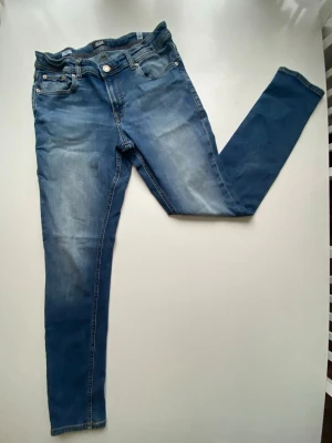 Blå jeans med slitningar - Säljer ett par blå skinny jeans med lätt slitna detaljer och klassisk femficksdesign. Jeansen har normal midja och smal passform hela vägen ner. Materialet är stretchigt denim som ger en bekväm känsla och snygg look.