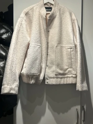 Krämvit jacka från PIECES - Säljer en krämvit jacka från PIECES med oversized passform och stora framfickor. Jackan har tryckknappar framtill, ribbad nederkant och mjukt, fluffigt material som ger en mysig look. Perfekt för dig som gillar stilrena och bekväma plagg.