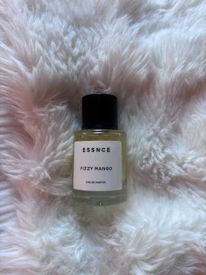 Essnce Fizzy Mango Eau de Parfum - Fräsch parfym från Essnce med doft av Fizzy Mango. Flaskan är rund och transparent med en svart cylinderformad kork och vit etikett. Perfekt för dig som gillar fruktiga och energiska dofter.
