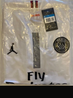  PSG 2019 x Jordan fotbollströja - Helt ny! Säljer en vit fotbollströja från samarbetet mellan Jordan och Paris Saint-Germain. Tröjan har svarta detaljer, PSG-logga på bröstet, Jordan-logga och texten 'Fly' framtill. Klassisk krage med rödblå rand upptill.