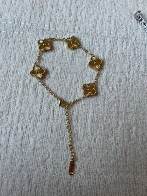 Guldpläterad armband med fyrklöver 18+5cm - Snyggt armband från Guess i guldfärg med fem dekorativa fyrklöverformade länkar. Armbandet har en tunn kedja och justerbar längd med en liten bricka där det står Guess. Perfekt för dig som gillar detaljerade smycken med elegant touch.