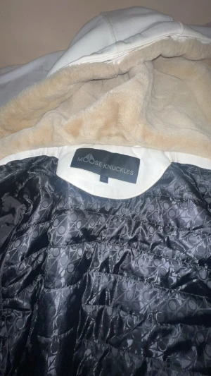 Vit classic bunny jacka  från Moose Knuckles - Säljer en vit Bunny jacka från Moose Knuckles med mjukt beige foder och quiltad svart insida med mönster. Jackan har huva och ribbade muddar vid ärmslut och nederkant. Perfekt för kalla dagar och har en clean look. Köpte jackan för 7 månader sen och den har fortfarande väldigt bra skick. Jag kan diskutera pris och kvitto finns även på jackan. Vill helst göra en snabb affär den är i storlek L