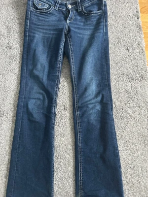 Blå bootcut jeans med kontrastsömmar - Säljer ett par klassiska blå bootcut jeans med vita kontrastsömmar. Jeansen har en lätt tvättad look och låg midja. Perfekta för dig som gillar en ett par hyfsat basic jeans men som ändå är fett snygga. Säljer då de e för korta.