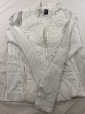 Vit quiltad jacka från SOC - Snygg vit jacka från SOC i storlek M. Jackan har quiltade partier framtill och på sidorna, ribbade muddar och dragkedja hela vägen. Perfekt för dig som gillar sportig och stilren look.