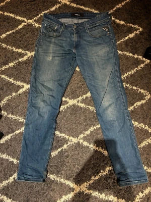 Replay byxor - Snygga blå slim fit jeans från Replay med klassisk femficksdesign och diskreta slitningar framtill. Jeansen har dragkedja och knapp i midjan samt detaljerade bakfickor med Replay-logga. Tillverkade i bomull med lite stretch för skön passform. Lite slitna men de syns på bilden