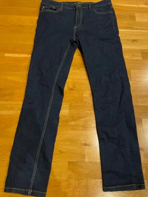Mörkblå raka jeans med kontrastsömmar - Säljer ett par mörkblå jeans med raka ben och tydliga kontrastsömmar. Klassisk femficksmodell med bälteshällor och knappgylf. Jeansen har en enkel och tidlös look som passar till det mesta. Materialet är denim i bomull. Stolek W31 L32