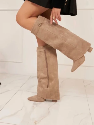 Beige knähöga boots i mockaimitation - Säljer ett par snygga beige knähöga boots i mockaimitation med spetsig tå och dekorativt spänne upptill. Dragkedja på insidan för enkel påtagning. Nästan aldrig använda 