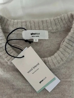 Beige stickad tröja från Gina Tricot - Mysig beige stickad tröja från Gina Tricot i ullblandning. Tröjan har rund halsringning, långa ärmar och ribbade muddar vid hals, ärmslut och nederkant. Perfekt för lager på lager och en clean look.