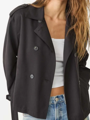 Stradivarius Kort svart trenchcoat med bälte - Slutsåld snygg jacka från stradivarius. Stilren svart trenchcoat i kort modell med dubbelknäppning, axelklaffar och bälte i midjan. Jackan har klassisk krage och knappar vid ärmsluten. Perfekt för dig som gillar en tidlös look med modern twist.