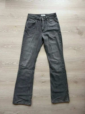 Grå bootcut  jeans från Gina Tricot - Snygga grå jeans från Gina Tricot med bootcut och klassisk femficksdesign. Jeansen har en diskret tvättad look och är tillverkade i ett mjukt denimtyg. Perfekta för en avslappnad och trendig stil.