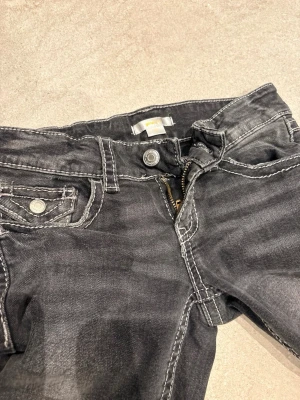 Svarta jeans från Gina Tricot - Snygga svarta jeans från Gina Tricot med slitna detaljer och kontrastsömmar. Klassisk femficksmodell med dragkedja och knapp i midjan. Perfekta för en trendig och avslappnad look.