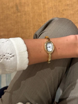 Guldfärgad armbandsklocka med nytt batteri - Stilren guldfärgad armbandsklocka med oval urtavla och romerska siffror i timex stuk. Klockan har ett smalt, elegant armband i guldfärgad metall  för dig som gillar klassisk och tidlös design. Precis bytt batteri så den fungerar som den ska☺️