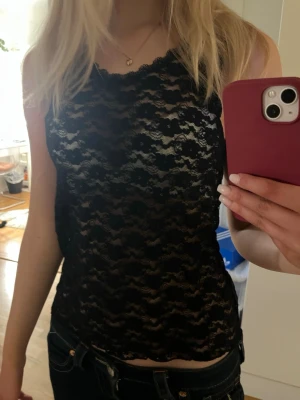 Svart spetslinnetopp med vågmönster - Snygg svart ärmlös linnetopp i spets med vågigt mönster. Toppen är lätt transparent och har en croppad passform som passar perfekt till  jeans eller kjol. Perfekt för dig som vill ha en trendig och edgy look.